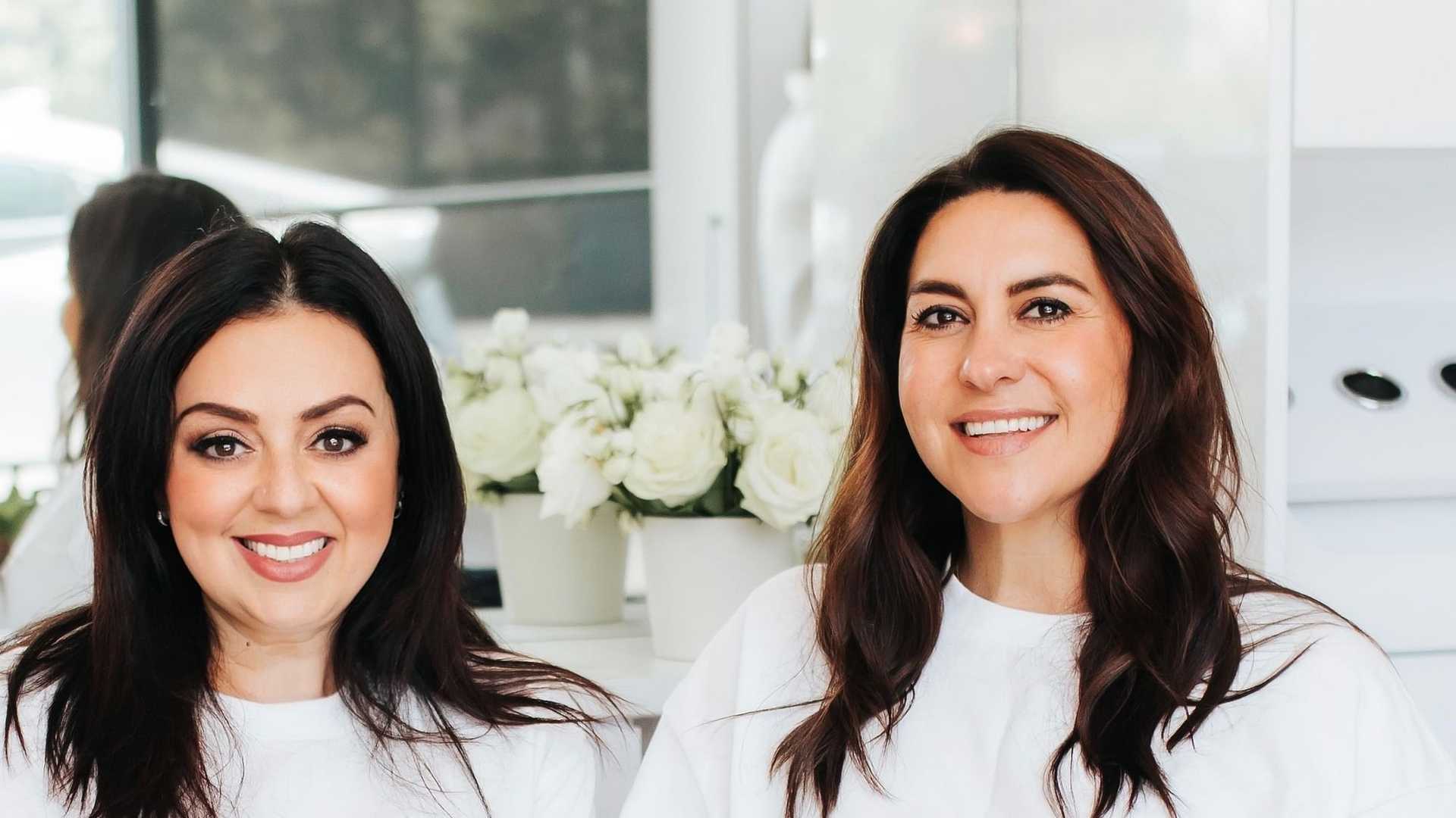 Two women in Rêve Salon shirts, smiling and seated in a stylish salon setting.